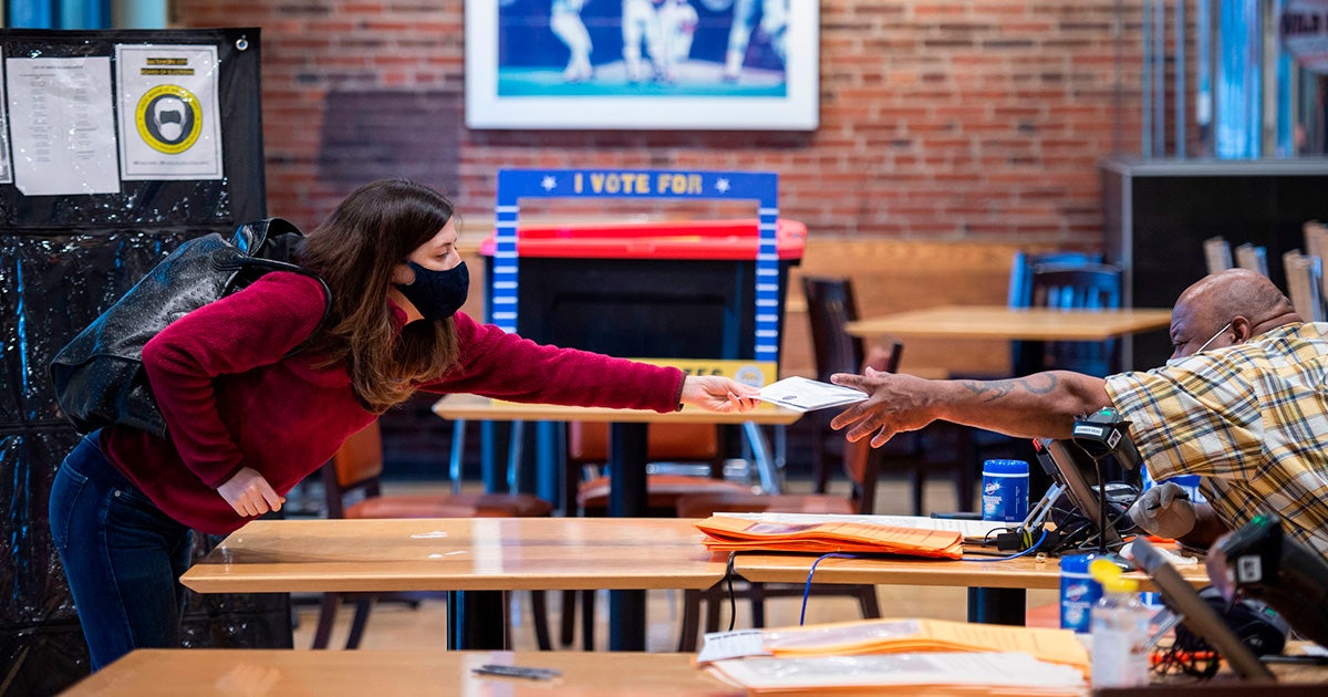 A volunteer (right) helps a woman register at an early voting station at Camden Yards, on the second day of early voting in Baltimore, Maryland, on October 27, 2020.