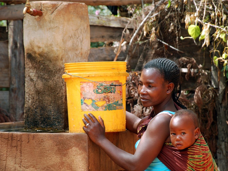 A woman carrying her child in Tanzania fills a bucket with water at a well.